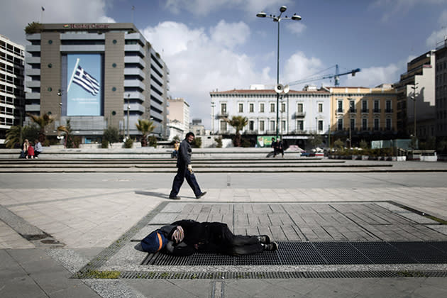 A pedestrian walks by as a homeless man sleeps on a metro air vent in Athens. (AP Photo/Petros Giannakouris)