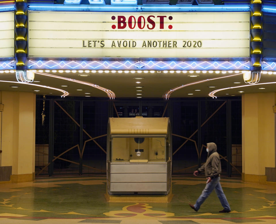 FILE - A man walks underneath the marquee of the Alex Theatre in Glendale, Calif., which bears a message urging people to get COVID-19 vaccine booster shots, Monday, Jan. 24, 2022. The omicron wave that assaulted the United States this winter also bolstered its defenses, leaving enough protection against the coronavirus that future spikes will likely require much less — if any — dramatic disruption to society. (AP Photo/Chris Pizzello, File)