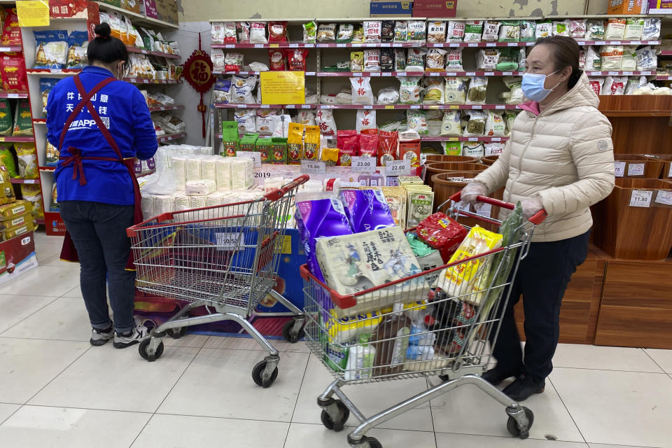 A woman wearing a mask pushes a carriage near a sign calling for shoppers to be vigilant against the coronavirus rebounding, not to listen to rumors and to avoid stockpiling at a supermarket in Beijing, China, Wednesday, Nov. 3, 2021. A recent seemingly innocuous government recommendation for Chinese people to store necessities for an emergency quickly sparked scattered instances of panic-buying and online speculation of imminent war with Taiwan. (AP Photo/Ng Han Guan)