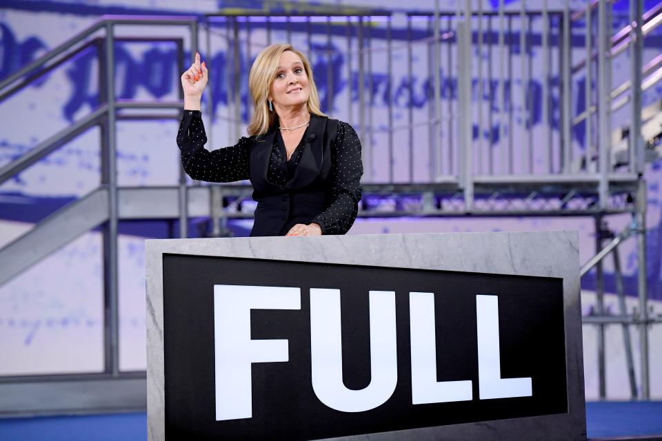 Samantha Bee looks gorgeous on stage with her right hand suspended in the air. 