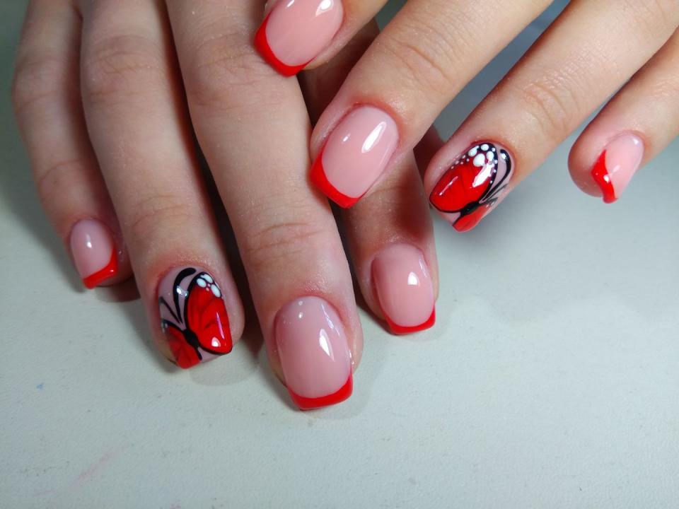 <p>These nude nails with red tips have a surprise—a statement nail with a bright-red butterfly on the ring fingers.</p>