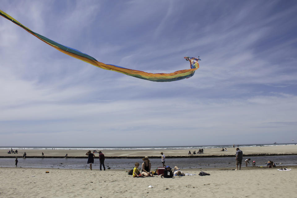 In this Thursday, May 28, 2020, photo Gwen Partlow and her sons, Cameron, 5, and Casey, 2, fly a kite on the beach during the coronavirus outbreak in Cannon Beach, Ore. With summer looming, Cannon Beach and thousands of other small, tourist-dependent towns nationwide are struggling to balance fears of contagion with their economic survival in what could be a make-or-break summer. (AP Photo/Gillian Flaccus)