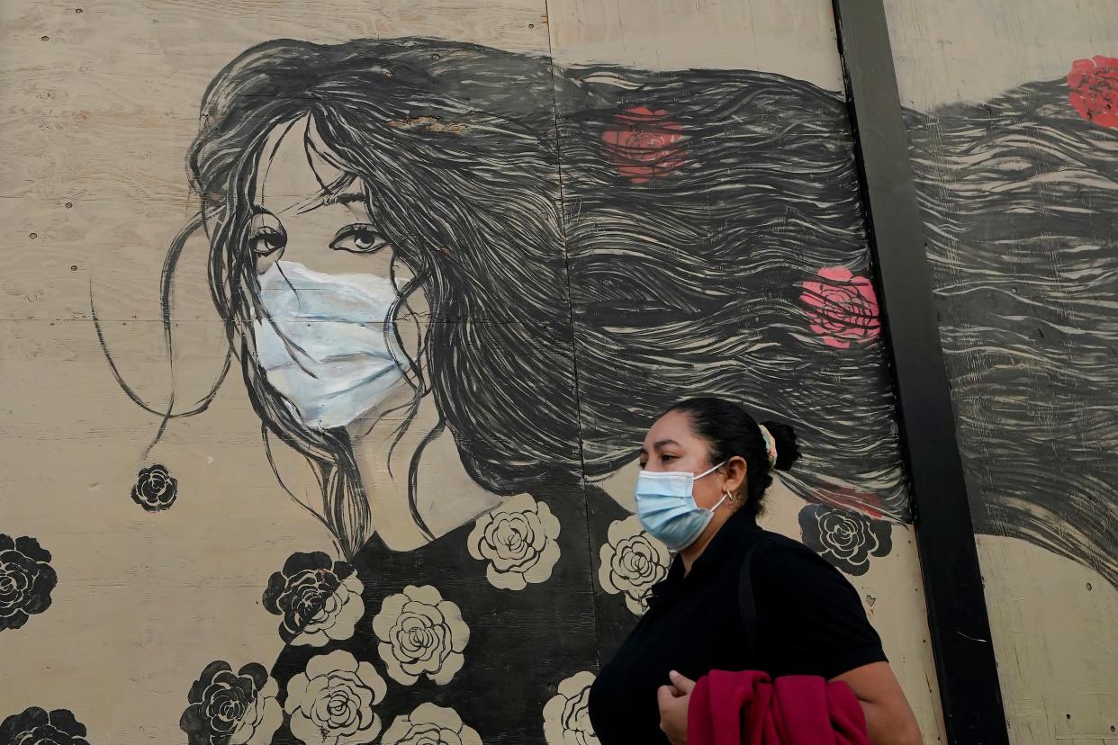 A woman wears a mask while walking past a mural of a woman in a mask during the coronavirus outbreak in San Francisco, Tuesday, Oct. 20, 2020.
