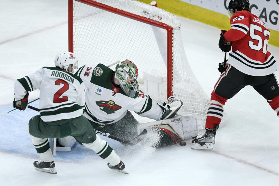 Minnesota Wild goalie Filip Gustavsson (32) makes a save against Chicago Blackhawks' Reese Johnson (52) while teammate Calen Addison (2) looks on during the second period of an NHL hockey game Monday, April 10, 2023. (AP Photo/Paul Beaty)