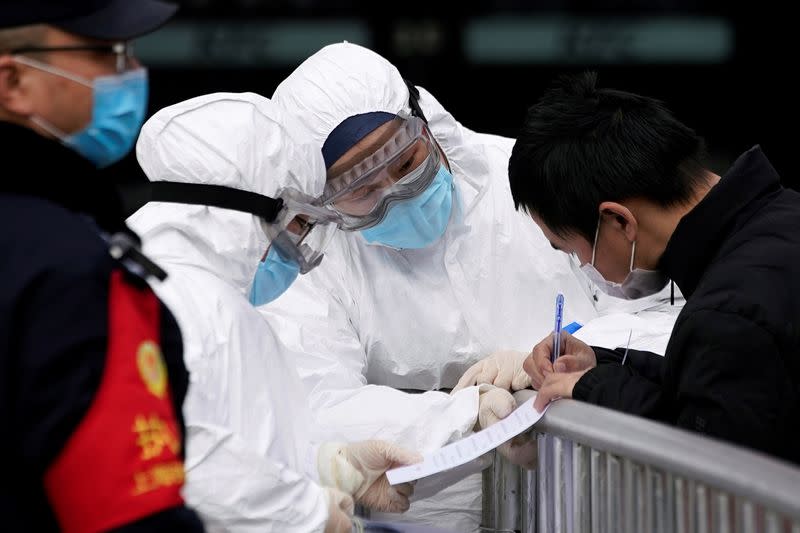 Staff members wearing protective masks check a passenger at Shanghai railway station in Shanghai