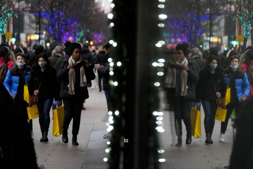 Shoppers are reflected in a window as they walk down Oxford Street, Europe's busiest shopping street, in London, Thursday, Dec. 23, 2021. The British government says it won’t introduce any new coronavirus restrictions until after Christmas, and called early studies on the severity of the omicron variant encouraging. (AP Photo/Frank Augstein)