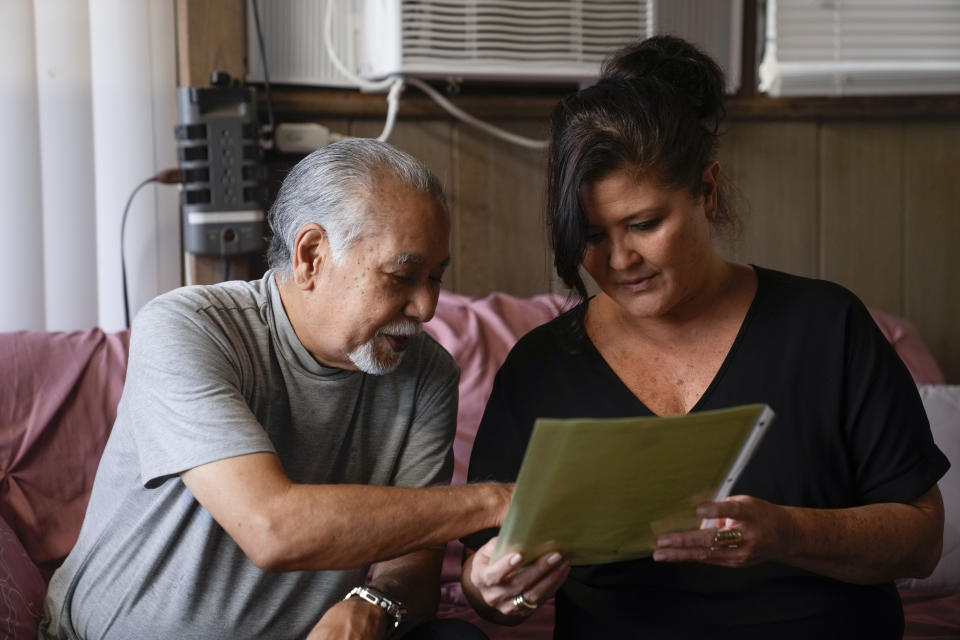 Weslee Chinen looks at the updated death certificate for his wife Sharlene Rabang, who was named as the 100th victim of the Lahaina wildfires, with Rabang's daughter Lorine Lopes, right, Tuesday, Dec. 5, 2023, at his family home in Waipahu, Hawaii. (AP Photo/Lindsey Wasson)