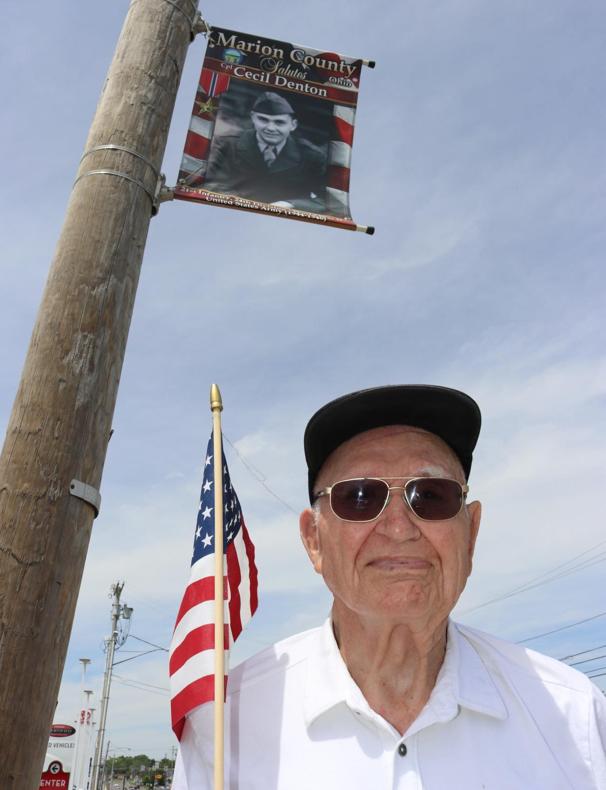 World War II veteran Cecil Denton stands under his banner located near Wendy's on Mount Vernon Avenue during the Stand by Your Veterans event on Saturday, May 27, 2023, ahead of the Memorial Day observance. The next Stand by Your Veterans event is set for Saturday, July 1. Family and friends of veterans whose images are on the banners displayed around Marion are asked to stand by the banners from 11:30 a.m. to 12:30 p.m. on July 1 to honor the veterans.