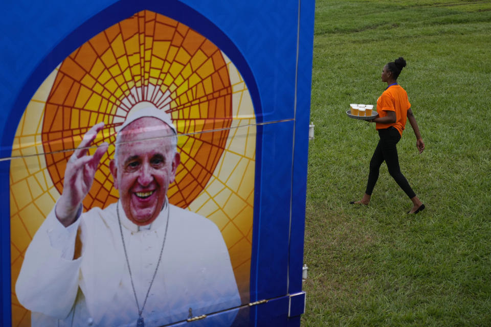 A woman walks past to a banner welcoming Pope Francis to Democratic Republic of Congo, at the "Palais de la Nation" in Kinshasa, Democratic Republic of the Congo, Tuesday, Jan. 31, 2023. Pope Francis starts his six-day pastoral visit to Congo and South Sudan where he'll bring a message of peace to countries riven by poverty and conflict. (AP Photo/Gregorio Borgia)