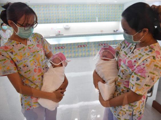 Nurses at Praram 9 Hospital in Bangkok hold two babies wearing face shields (AFP/Getty)