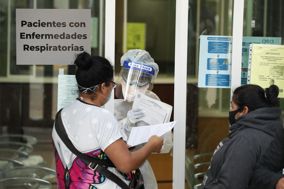 A medical worker in protective gear speaks to women wearing masks at the door of the ward designated for respiratory emergencies, at Dr. Manuel Gea Gonzalez General Hospital, one of many treating patients with symptoms of the new coronavirus, in Mexico City, Wednesday, April 22, 2020. Several people waiting outside for news of their hospitalized relatives said their family members were being treated in the waiting room since yesterday, since beds in the respiratory ward were full. (AP Photo/Rebecca Blackwell)