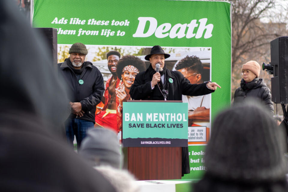 A man at a lectern in front of a sign saying death