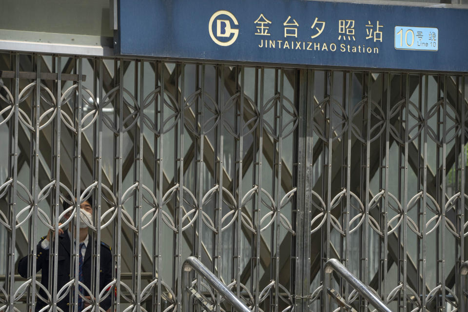 A worker wearing a face mask stands inside the gates of the closed exit of a subway station in Beijing, Wednesday, May 4, 2022. Beijing on Wednesday closed around 10% of the stations in its vast subway system as an additional measure against the spread of coronavirus. (AP Photo/Mark Schiefelbein)