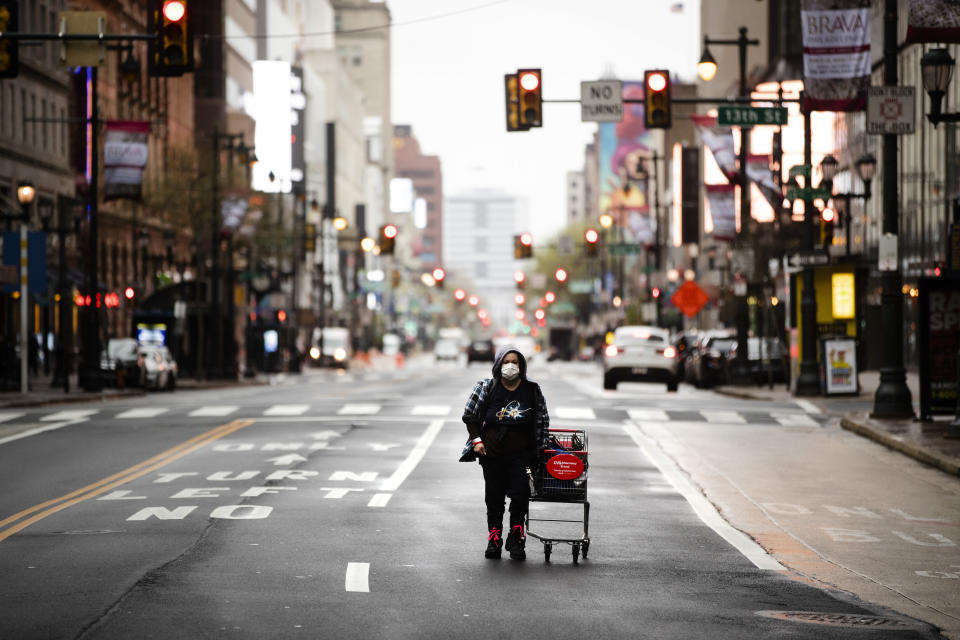 FILE - In this April 13, 2020, file photo a person wearing a protective mask walks down Market Street in Philadelphia. Across an arc of vital swing states, the coronavirus has put politics on an uneasy pause. Political fights are raging among state leaders from Iowa to Pennsylvania over the handling of the pandemic’s impact. (AP Photo/Matt Rourke, File)