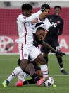 Canada's Cyle Larin, center, falls under a challenge from United States' Yunus Musah, left, and teammate Miles Robinson, right, during the first half of a World Cup soccer qualifier in Hamilton, Ontario, Sunday, Jan. 30, 2022. (Frank Gunn/The Canadian Press via AP)