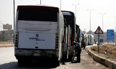 A driver stands next to a bus as he waits to cross into the town of Douma, eastern Ghouta, to evacuate rebels and their families, at Wafideen camp in Damascus, Syria April 1, 2018. REUTERS/Omar Sanadiki