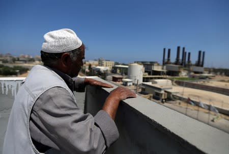 Palestinian man looks out of his house as the Gaza power plant is seen, in the central Gaza Strip