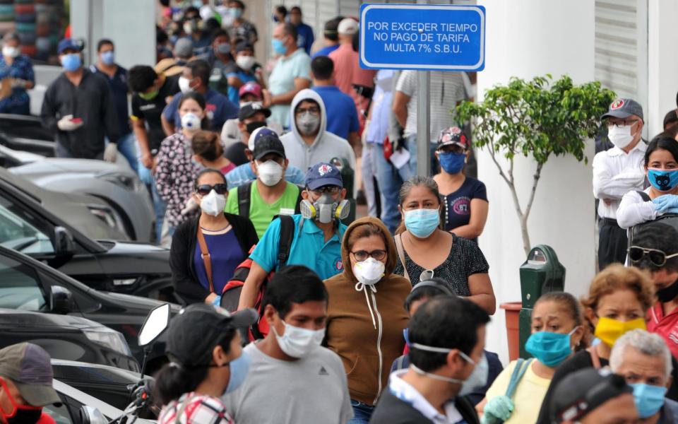 People wear face masks as they wait in line outside a bank in Guayaquil on April 28 - AFP