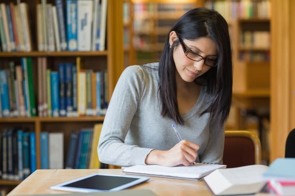 Woman sitting in a library, writing on a notebook