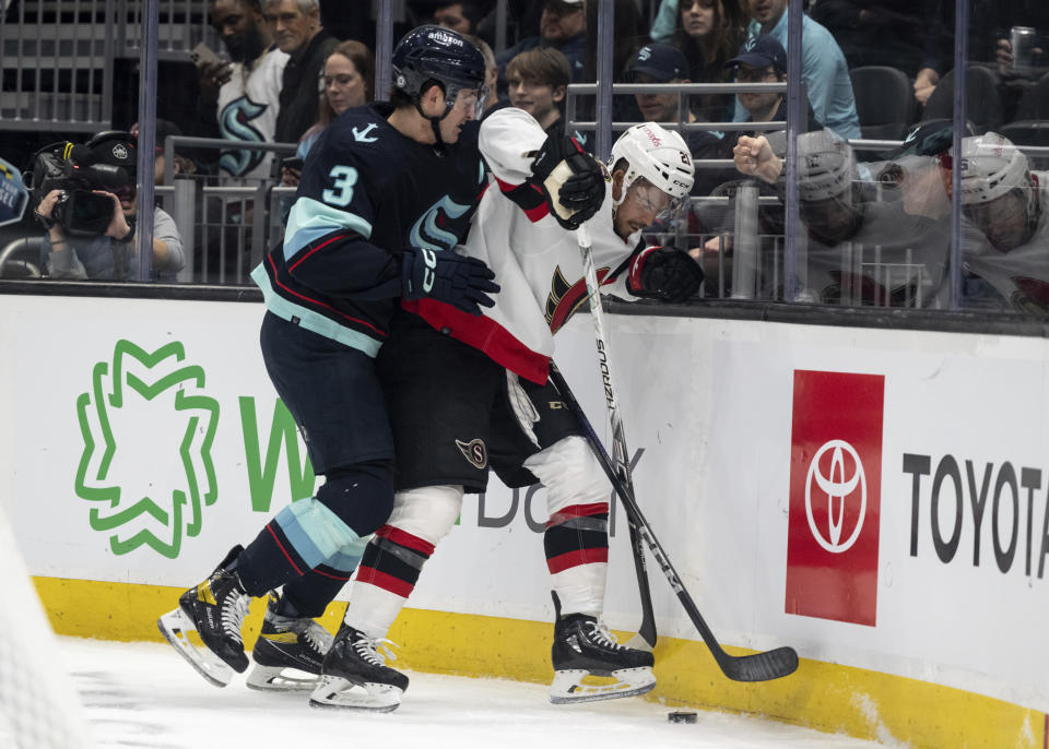 Ottawa Senators forward Mathieu Joseph, right, and Seattle Kraken defenseman Will Borgen compete for the puck along the boards during the first period of an NHL hockey game Thursday, March 9, 2023, in Seattle. (AP Photo/Stephen Brashear)