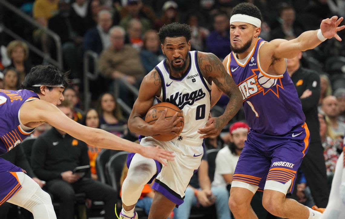 Sacramento Kings guard Malik Monk (0) drives by Phoenix Suns forward Yuta Watanabe (18) and Phoenix Suns guard Devin Booker (1) during the second half Friday, Dec. 8, 2023, at Footprint Center in Phoenix, Arizona.