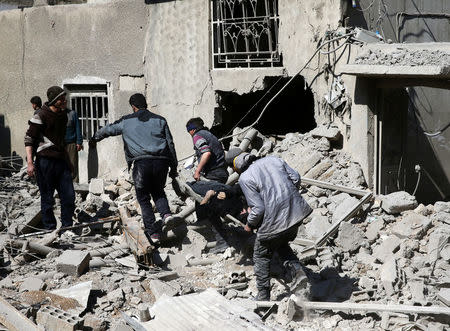 People carry a body on a stretcher as they walk on rubble of damaged buildings in the rebel held besieged town of Hamouriyeh, eastern Ghouta, near Damascus, Syria, February 21, 2018. REUTERS/Bassam Khabieh