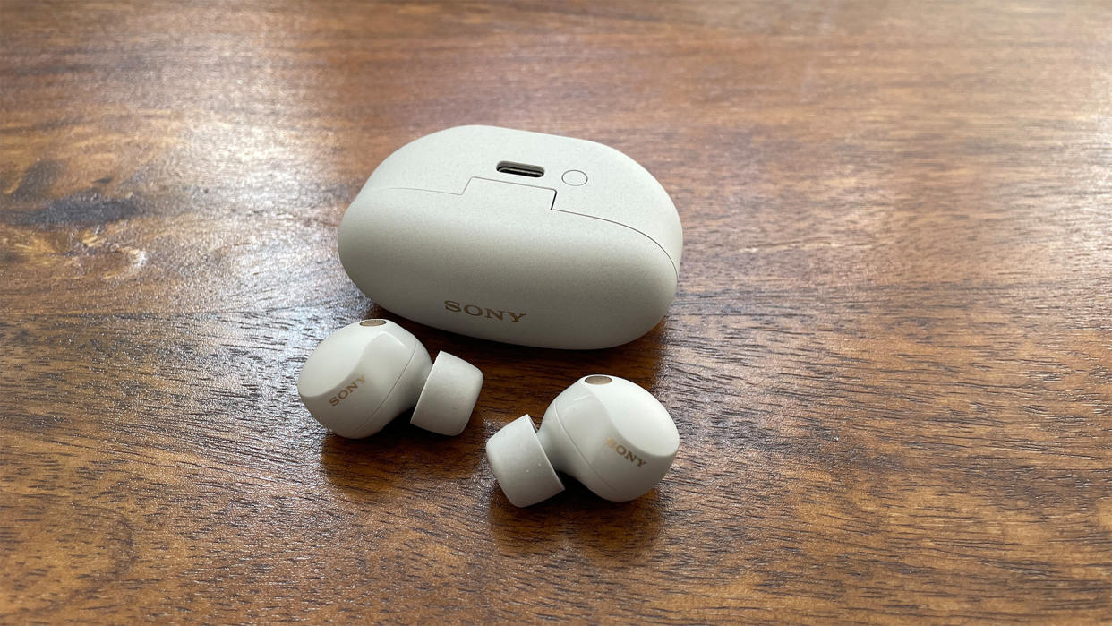  Sony WF-1000XM5 true wireless earbuds in white with their charging case on a table. 