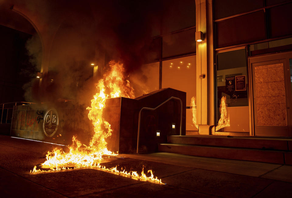 Demonstrators set fire to the front of the California Bank and Trust building during a protest against police brutality in Oakland, Calif., on Friday, April 16, 2021. (AP Photo/Ethan Swope)