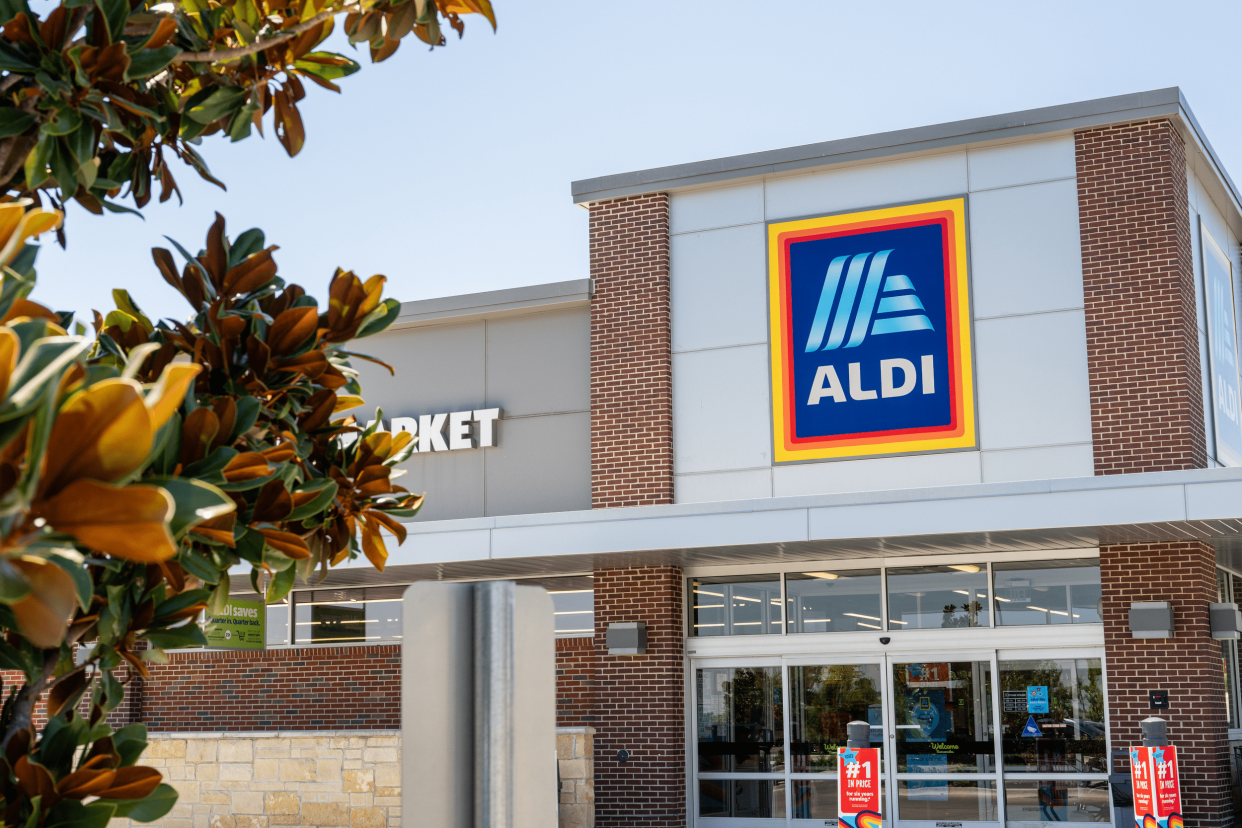 Front exterior of an Aldi grocery store, Pflugerville, Texas, decorative bush in the left foreground, on a sunny day