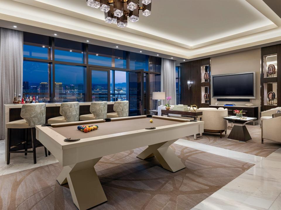 a game room with a bar, billiards by a living room next to a large floor to ceiling window with views of Las Vegas