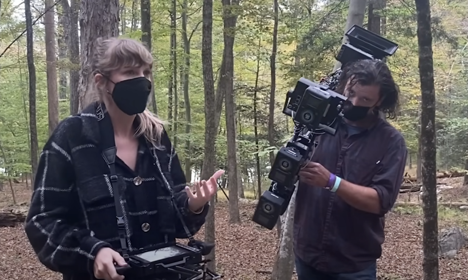 Woman and man outdoors with camera rig, both focused on equipment. Woman gestures as if explaining