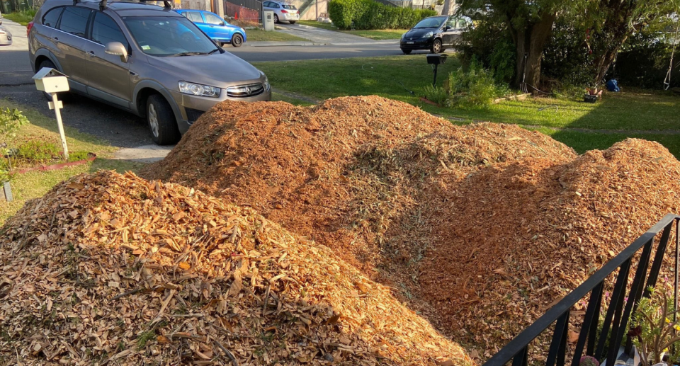 Image of mounds of mulch in front of a house with a car in the background. 