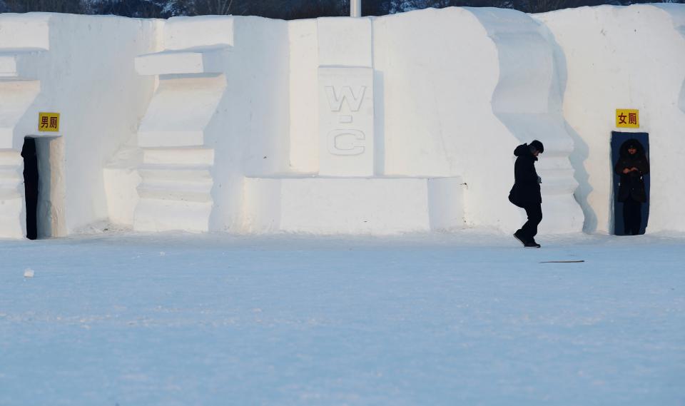 A woman leaves a toilet which has been decorated into a snow sculpture at the Harbin International Snow Sculpture Art Expo in Harbin