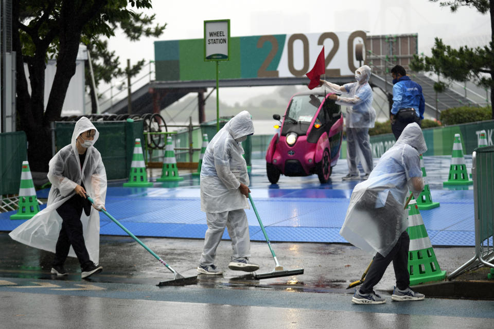 Staff wipe off rain water from the competition site prior to the women's triathlon competition at the 2020 Summer Olympics on Tuesday, July 27, 2021, in Tokyo, Japan. (AP Photo/Eugene Hoshiko)