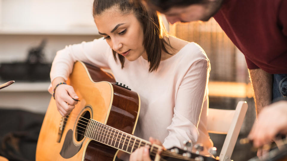 Young man teaching a teenage girl to play the guitar.