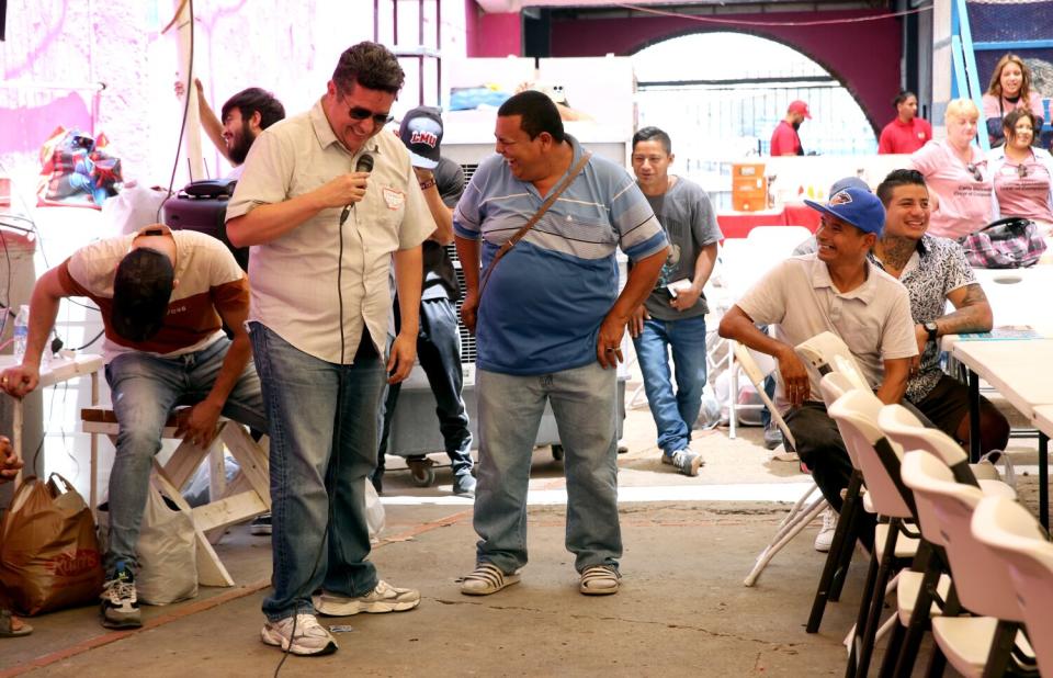 A man stands and talks near several men standing and sitting at tables.