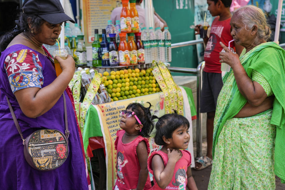 Women sip cool drinks as little girls wait for their turn at a roadside stall in Kolkata, India, Friday, May 3, 2024. (AP Photo/Bikas Das)
