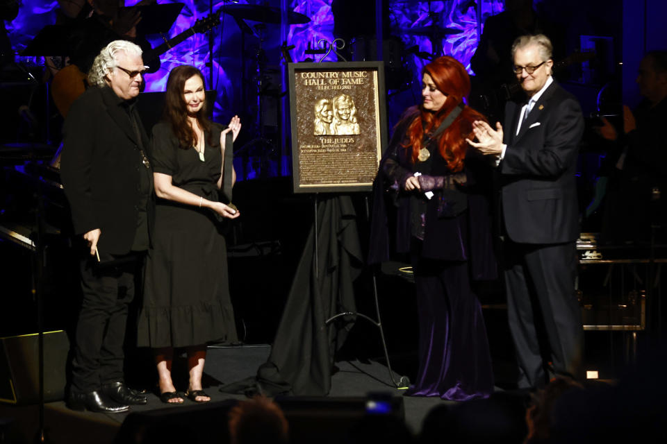 FILE - Wynonna Judd, second from the right, stands next to the Judds' induction plaque as sister Ashley Judd, left, Ricky Skaggs, and MC Kyle Young, CEO of the Country Music Hall of Fame & Museum look on during the Medallion Ceremony in Nashville, Tenn., on May 1, 2022. Fans of Naomi Judd, the late matriarch of the Grammy-winning country duo, will have a chance to say goodbye and rejoice in their hits in a final tour helmed by daughter Wynonna and all-star musical partners. (Photo by Wade Payne/Invision/AP, File)