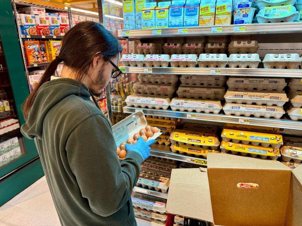 person wearing ponytail green hoodie medical gloves inspects eggs in grocery story