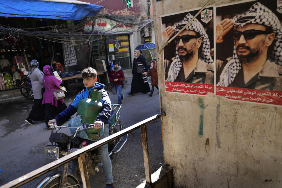 A Palestinian boy carries a gas canister on a motorcycle as he passes portraits of the late Palestinian leader Yasser Arafat, in the Bourj al-Barajneh Palestinian refugee camp, in Beirut, Lebanon, Tuesday, Jan. 18, 2022. The agency for Palestinian refugees, or UNRWA, appealed Wednesday to the international community to donate tens of millions of dollars to help improve living conditions for Palestinians in crisis-hit Lebanon. UNWRA is asking for an additional $87.5 million to provide Palestinian refugees with cash assistance to the poorest, cover hospital expenses, as well as transportation for children so that they can go to school. (AP Photo/Hussein Malla)