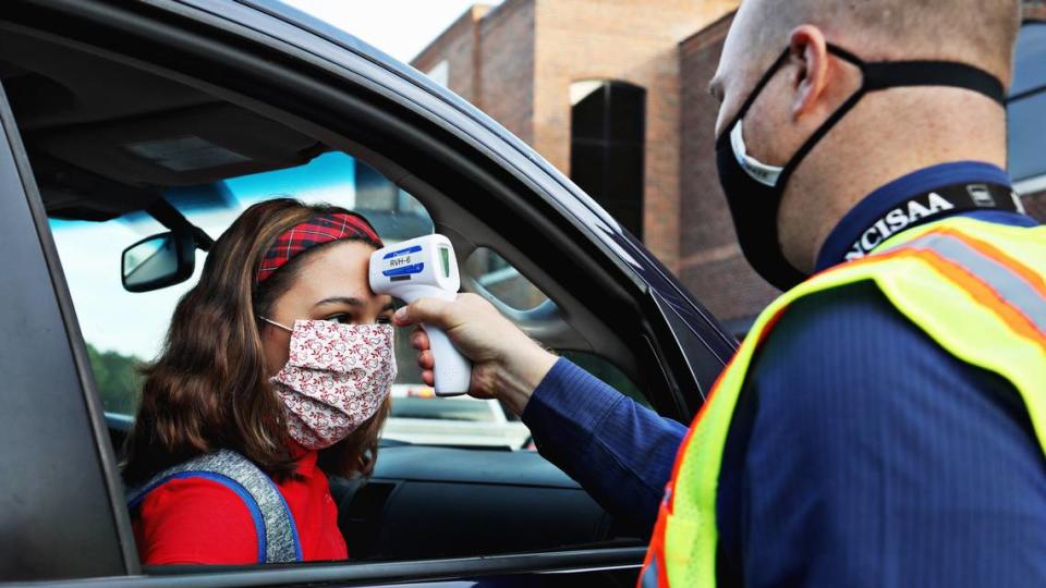 Seventh-grader Sophie Uvino, left, gets her temperature checked in carpool by Thales Academy American history teacher Nathaniel Johnston, right, before she can enter the school on July 22, 2020, in Rolesville.