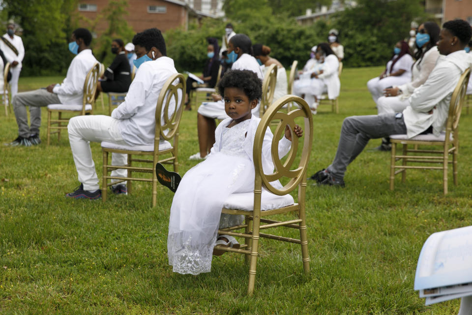 Amora, a grandchild of Joanne Paylor, 62, of southwest Washington, holds a fan with her grandmother's image on it during her outdoor memorial service at Cedar Hill Cemetery in Suitland-Silver Hill, Md., Sunday, May 3, 2020. Guests were seated in golden chairs six feet apart across the lawn to comply with social distancing rules. Despite not having died from coronavirus, almost every aspect of her funeral has been impacted by the pandemic. (AP Photo/Jacquelyn Martin)