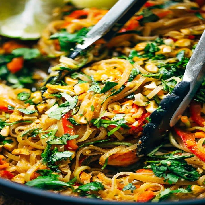 Tongs stirring a skillet full of vegetable pad Thai