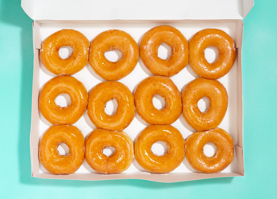 Overhead view of plain glazed doughnuts in a white delivery box on an aqua colored surface