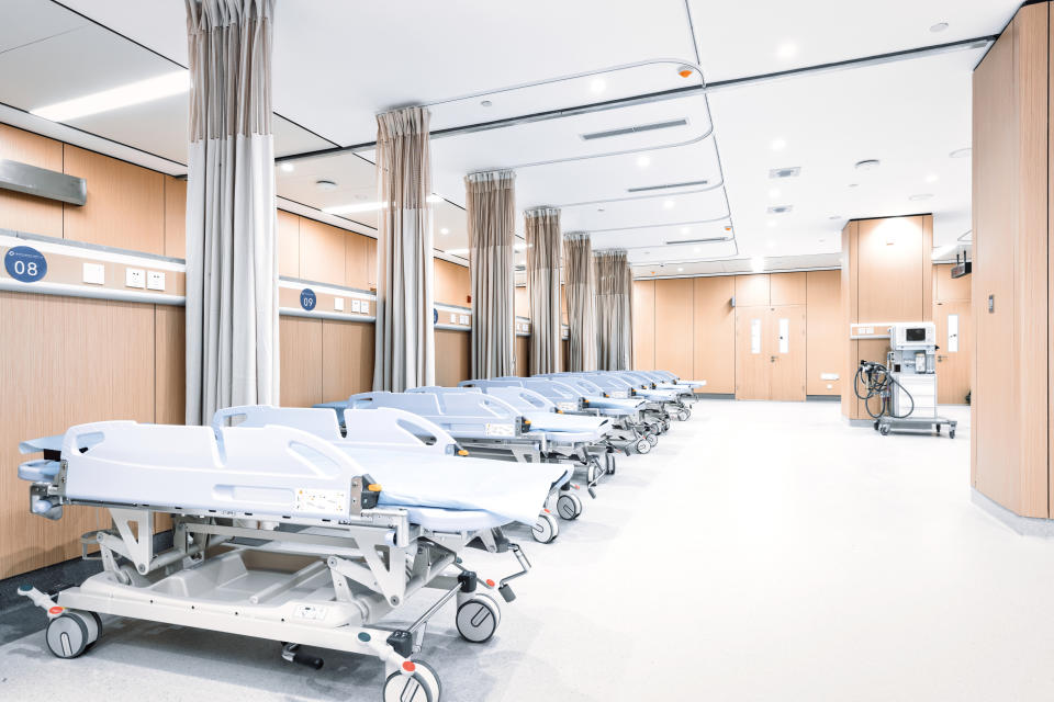 Hospital ward with an empty, modern setup. Multiple medical beds are lined up with privacy curtains in a clean, organized environment