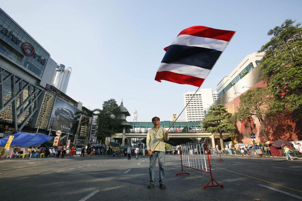 An anti-government protester waves a national flag at an occupied intersection in the main business district of Bangkok, Thailand, Wednesday, Jan. 29, 2014. The latest spasm in Thailand’s ongoing political upheaval is taking an economic toll as anti-government protesters barricade Bangkok's major intersections and confrontations between protesters and government supporters periodically flare into deadly clashes. (AP Photo/Wally Santana)