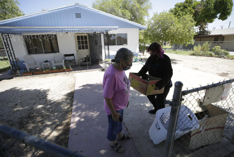 Marta Rosales, left, looks on as her daughter Erica Rosales takes a box of donated food from a neighbor into their house Thursday, July 23, 2020, in Brawley, Calif. Without Erica's paycheck from her work as a substitute teacher, the family has had to cut back everywhere, and gets by with the help of food donations and kind neighbors. (AP Photo/Gregory Bull)
