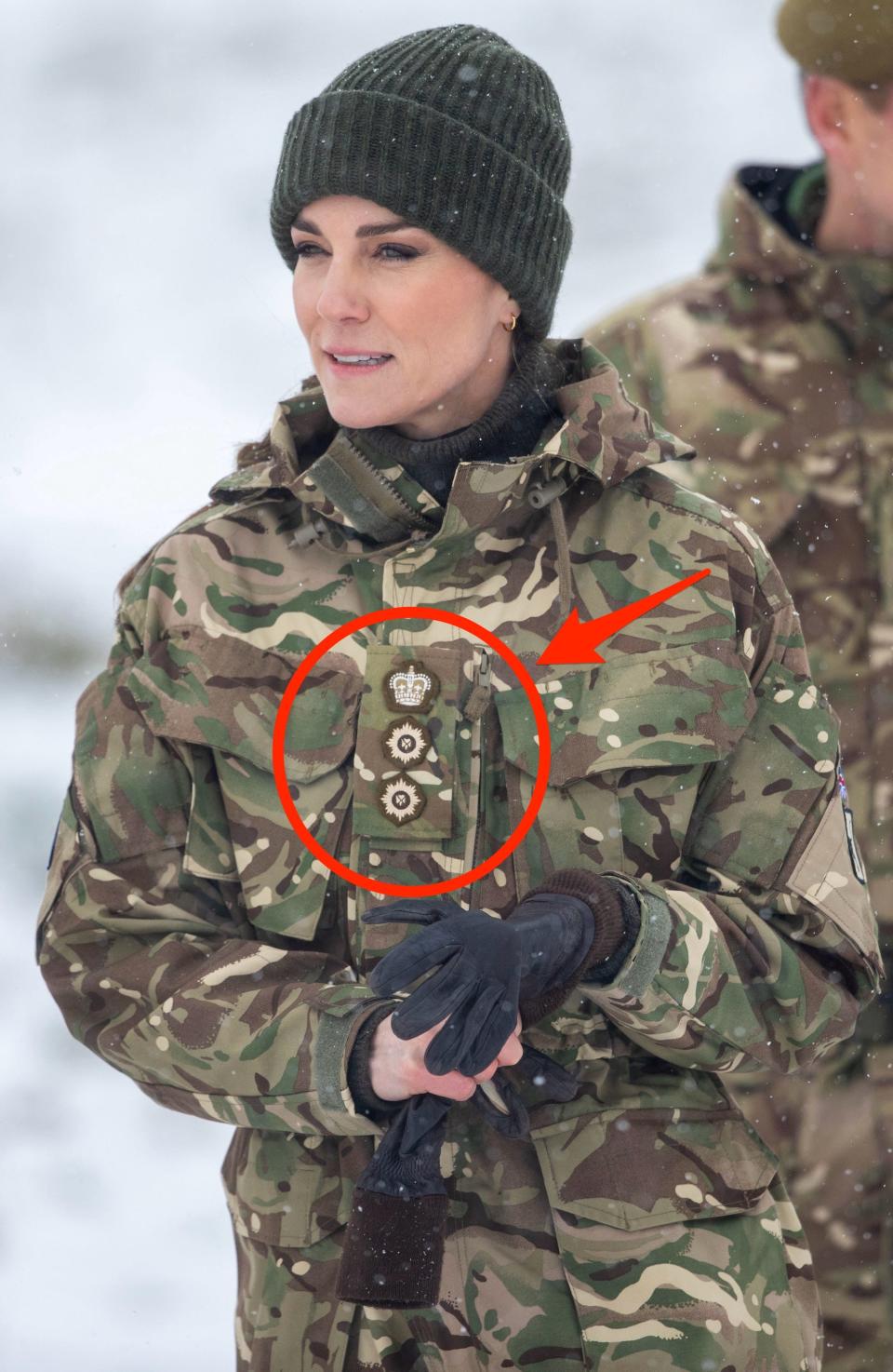 Kate Middleton wears camouflage in the snow. A red circle and arrow point to badges on her chest.