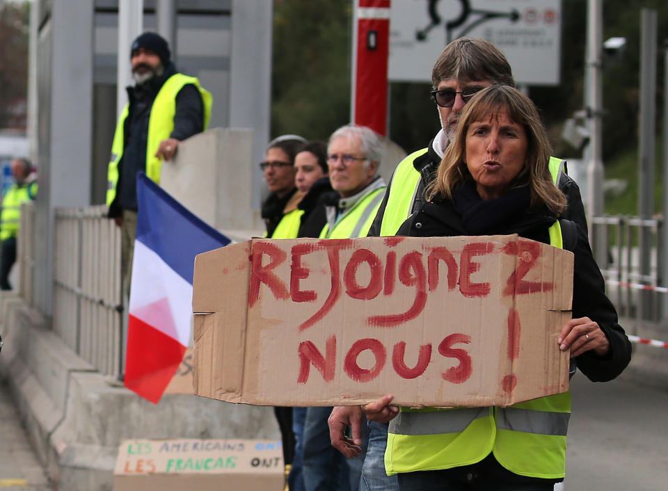A demonstrator holds a placard reading " Join us" as they stand by toll gates on a motorway at Biarritz southwestern France, Wednesday, Dec.5, 2018. The concessions made by French president Emmanuel Macron's government in a bid to stop the huge and violent anti-government demonstrations seemed on Wednesday to have failed to convince protesters, with trade unions and disgruntled farmers now threatening to join the fray. (AP Photo/Bob Edme)