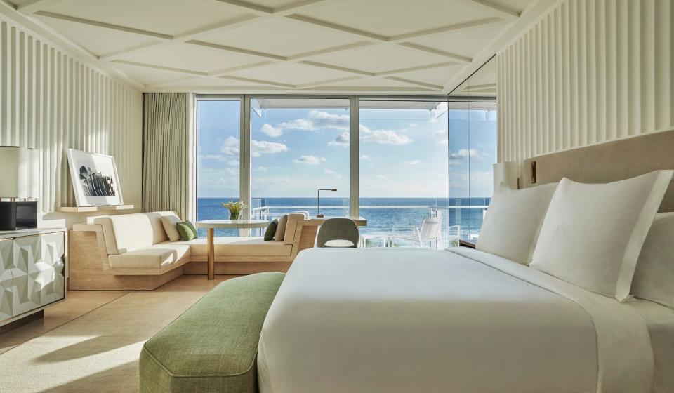 A white bed overlooking a floor-to-ceiling window with a view of the ocean.